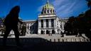 A person is silhouetted in the shade as they walk by the Pennsylvania Capitol in Harrisburg, Pa.